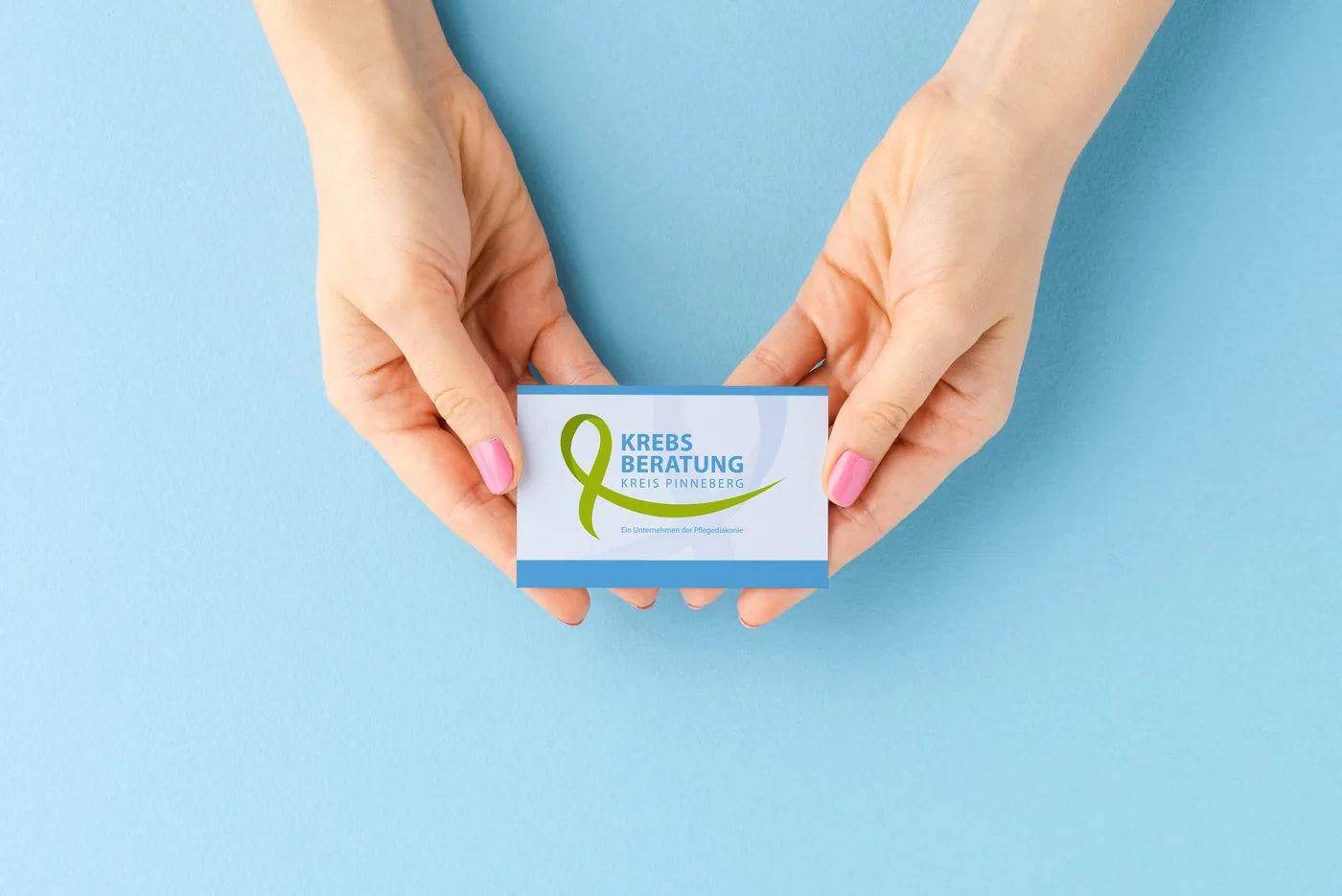 Zwei Hände halten eine Visitenkarte mit dem Logo der Krebsberatung Kreis Pinneberg, einem Unternehmen der Pflegediakonie.